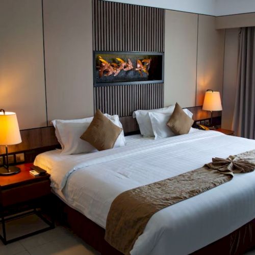 A cozy hotel room featuring a large bed, two bedside tables with lamps, a decorative wall panel, and a window with curtains.