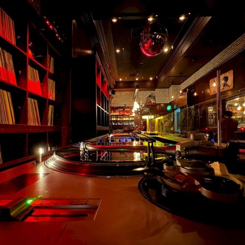 A cozy DJ booth with turntables, records on shelves, and ambient red lighting, creating a warm, inviting atmosphere in the space.