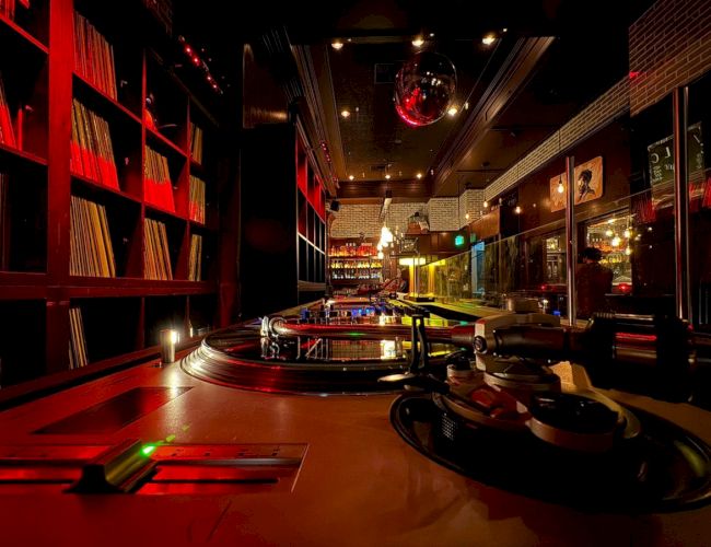 A cozy DJ booth with turntables, records on shelves, and ambient red lighting, creating a warm, inviting atmosphere in the space.