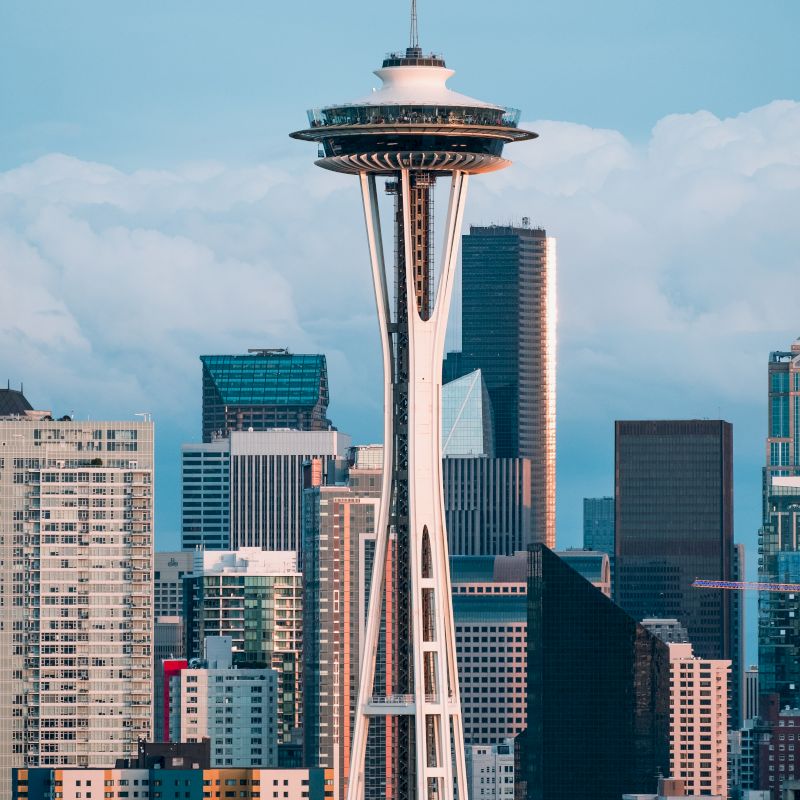 This image shows the Space Needle, a prominent observation tower, with a backdrop of modern skyscrapers in Seattle, Washington, under a cloudy sky.